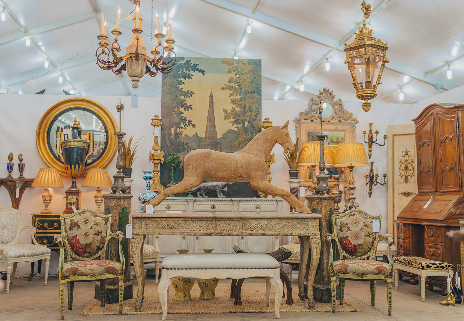 Antique furniture, chandeliers, ornate mirrors, and a wooden horse displayed at the Original Round Top Antiques Fair